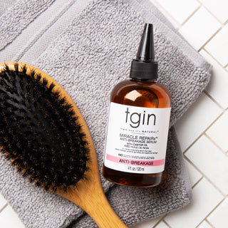 tgin Miracle RepaiRx Anti-Breakage Serum with boar bristle brush on gray towel