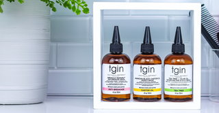 tgin Miracle RepaiRx Anti-Breakage Serum, Jamaican Black Castor Oil Growth Serum and Tea Tree and Olive Oil serum on a white shelf in a tiled bathroom