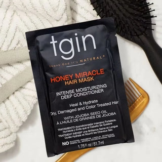 tgin Honey Miracle Hair Mask packet on a marble counter with a towel, brush and comb