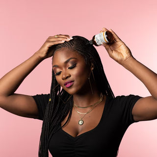 Woman with braids applying tgin hair serum to her scalp on a pink background