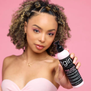 Woman with curly hair holding a tgin Rose Water product on a pink background