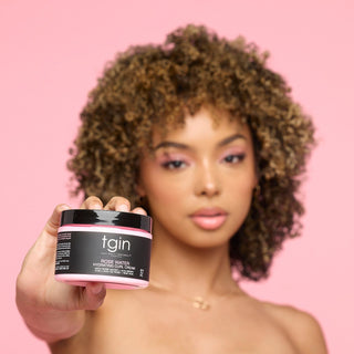 Woman with curly hair holding a jar of tgin Rose Water Hydrating Curl Cream toward the camera