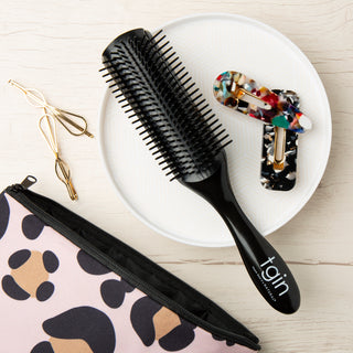 Black tgin styling brush on a white plate with hair clips and a leopard print pouch