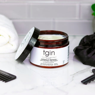 Open jar of tgin Miracle RepaiRx CPR Protein Treatment on a marble counter with a comb and towel