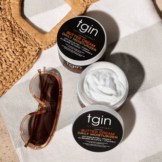 Two jars of tgin Butter Cream Daily Moisturizer, one open, on a striped towel with sunglasses and a woven bag