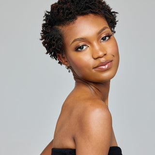 Woman with short coily twisted hair and a black strapless top posing against a gray background