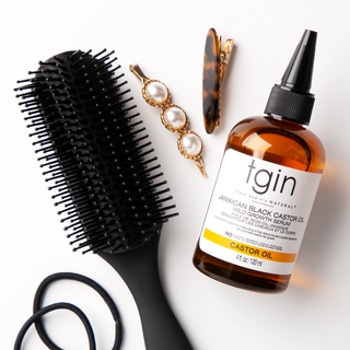 tgin Jamaican Black Castor Oil Growth Serum bottle with a hairbrush, hair clips, and hair ties