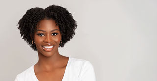 Smiling woman with short coily natural hair in a white top