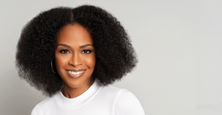 Smiling woman with full coily natural hair in a white top