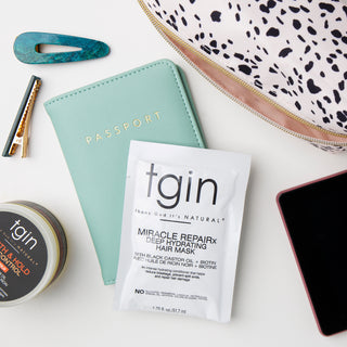 tgin Miracle RepaiRx Deep Hydrating Hair Mask packet with a passport cover, hair clips, and a tgin jar