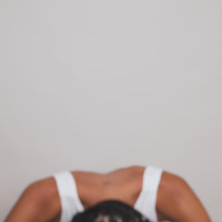 Video preview: person in a white tank top bent forward, top of head with dark hair visible, plain backdrop
