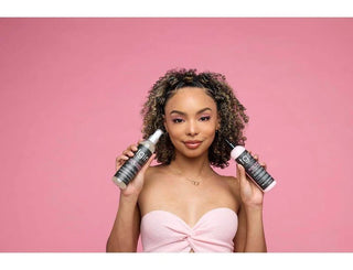 Woman with curly hair holding two tgin spray bottles on a pink background