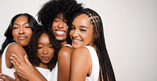 Four smiling women with curly, coily and braided natural hair in white tops