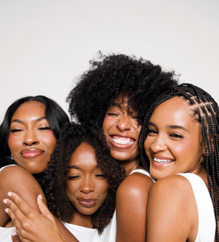 Four smiling women with curly, coily and braided natural hair in white tops